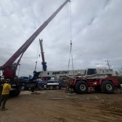 Two mobile cranes rigged on a muddy jobsite with a worker in a hi-vis vest in the foreground.