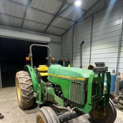 A green John Deere 5200 utility tractor parked under the lights inside the shop bay at night.