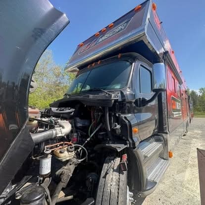 A black and red Freightliner race hauler with the hood tilted forward, exposing the engine for diagnosis.