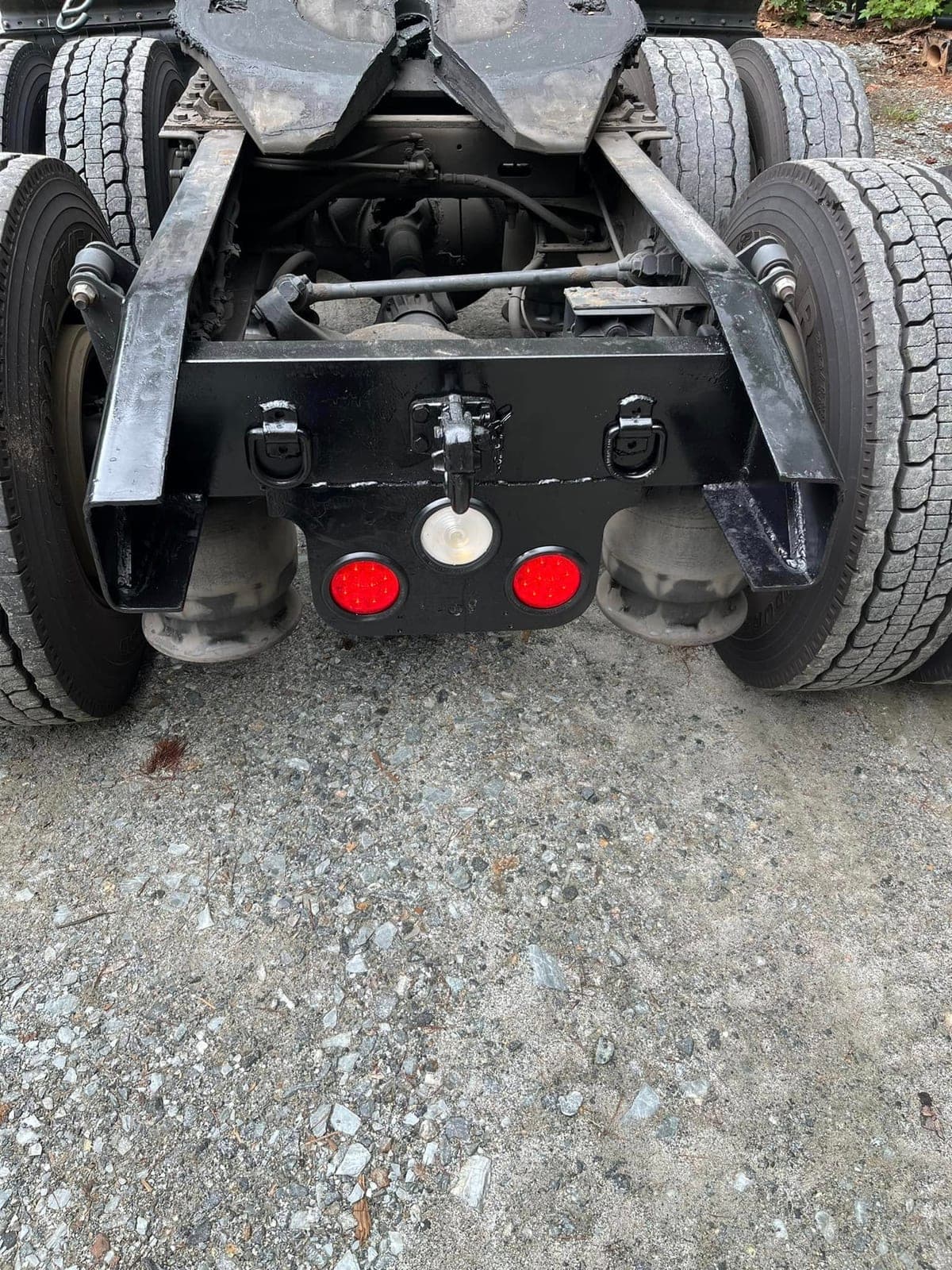 A freshly fabricated and painted rear crossmember welded into a truck frame, with tie-down D-rings, air bags and dual tires either side.
